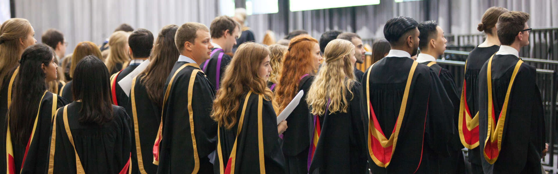 a line of graduands in convocation regalia are shown from behind