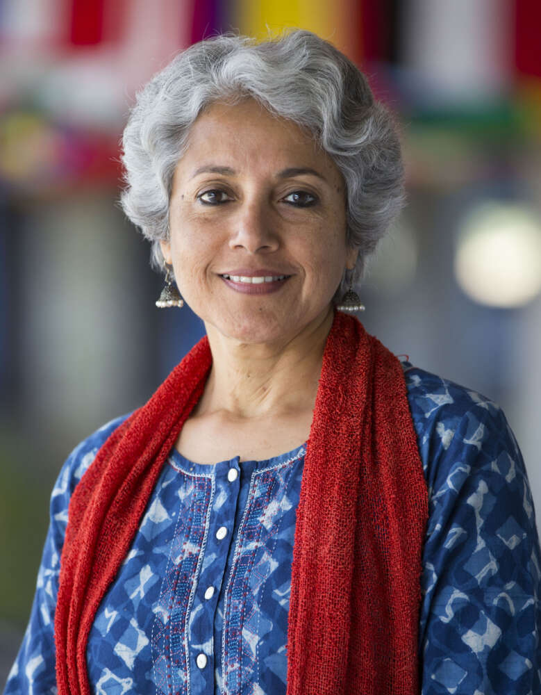 Dr. Soumya Swaminathan smiles and poses for a portrait with colourful flags behind her