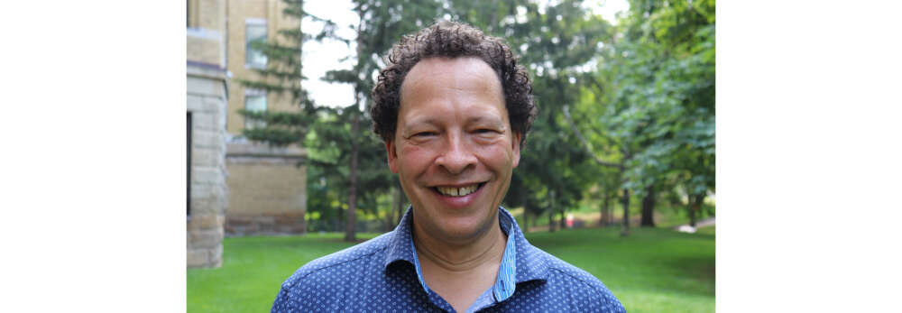 Lawrence Hill smiles for a portrait while standing outside with trees behind