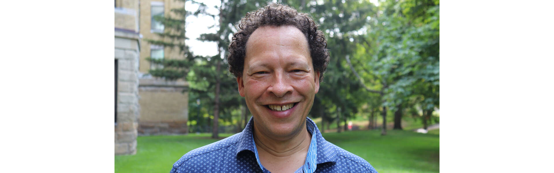 Lawrence Hill smiles for a portrait while standing outside with trees behind
