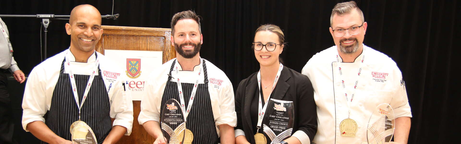 Four people stand in a row holding silver medals from a chef's competition.