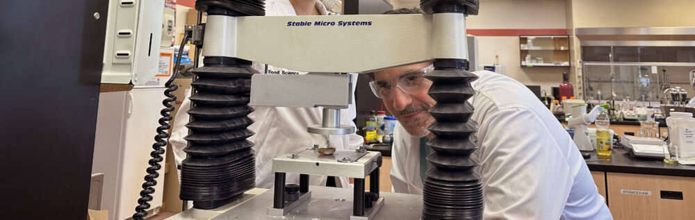 Two people in white lab coats peer through a machine known as a mechanical mouth