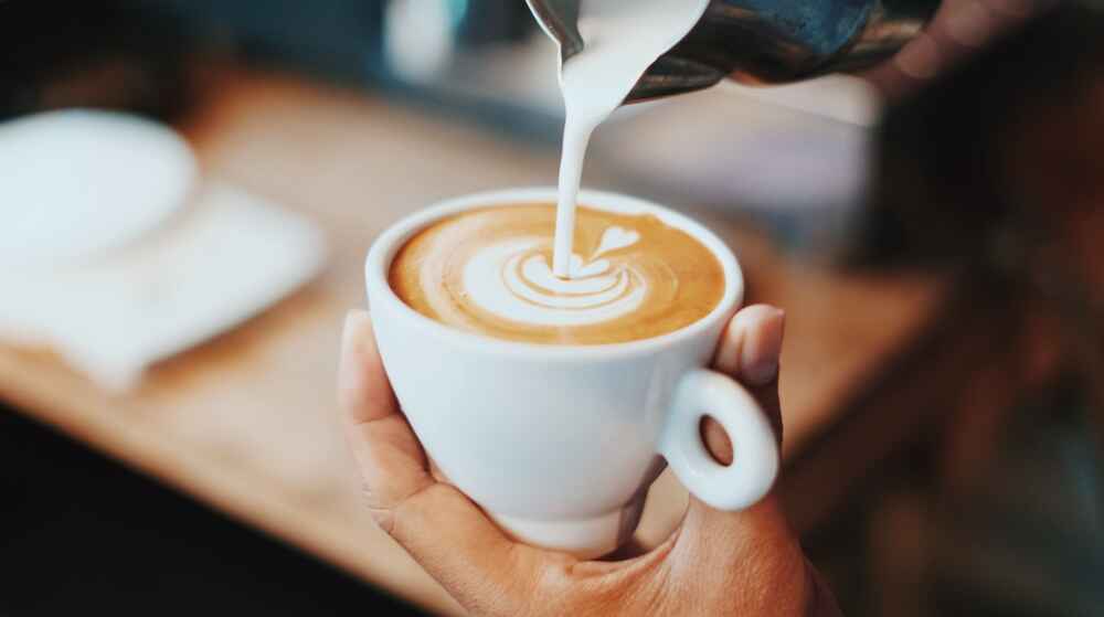 a hand holds a coffee cup while pouring in milk for latte art
