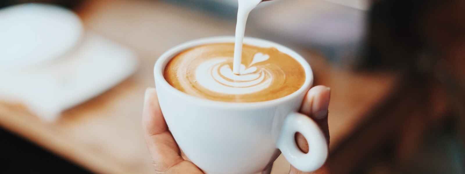 a hand holds a coffee cup while pouring in milk for latte art
