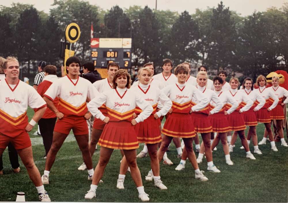 About 18 members of the Gryphons cheerleading squad stand on the football field with their hands on their hips