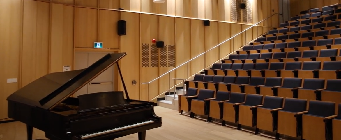 A grand piano sits in a theatre with dozens of seats rising above