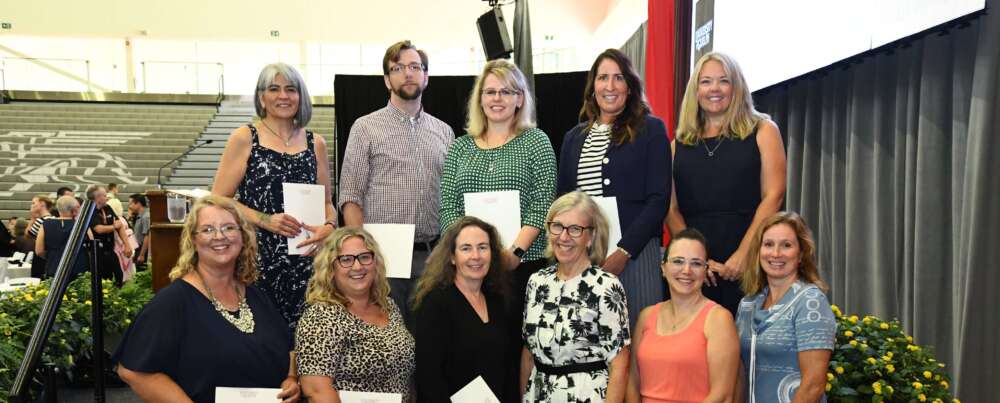 Two rows of U of G staff members stand together with President Dr. Charlotte Yates holding their exemplary staff awards.