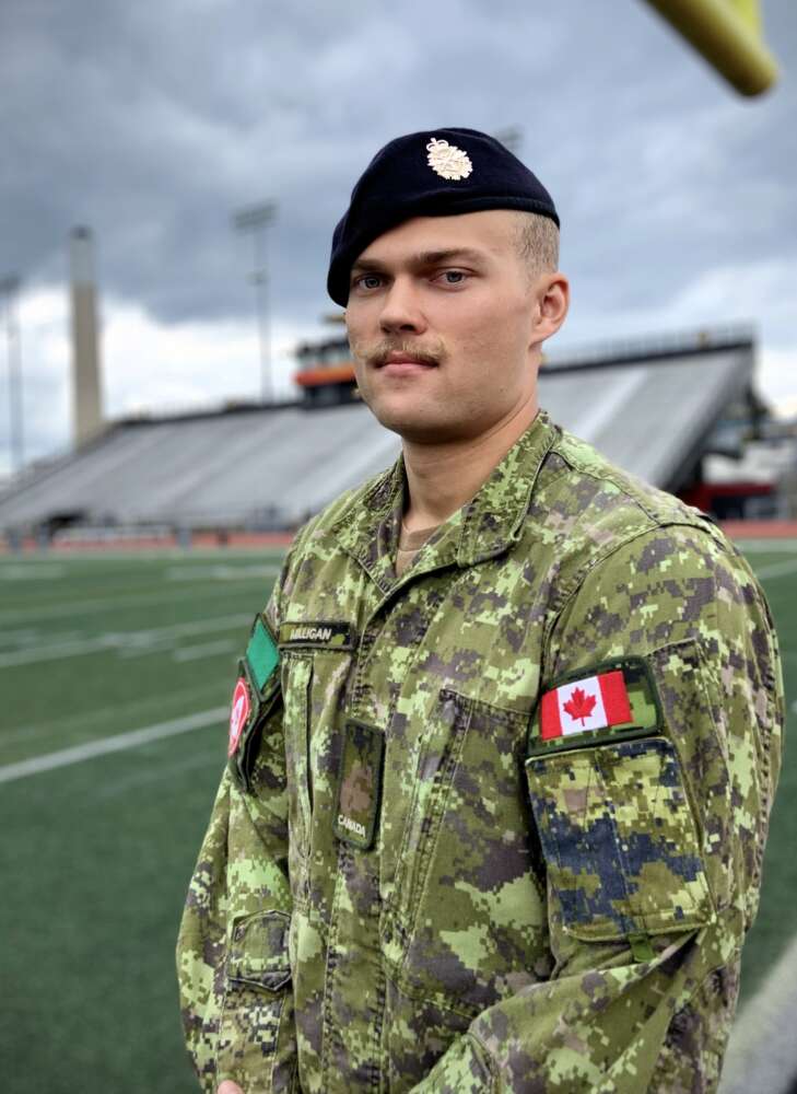 a reservist soldier stands in a camouflage-emblazoned operational uniform while standing on a football field