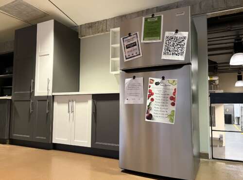 A stainless steel fridge with several notices affixed with magents near grey and white kitchen cabinetry