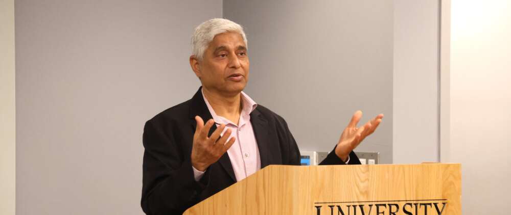 a man gestures with his hands while standing at a podium marked University of Guelph