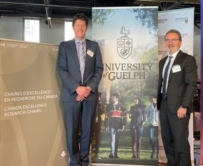 Dr. David McCarthy poses for a photo at the CERC announcement ceremony with Dr. Rene Van Acker beside banners for Canada Excellence Research Chair and the University of Guelph.