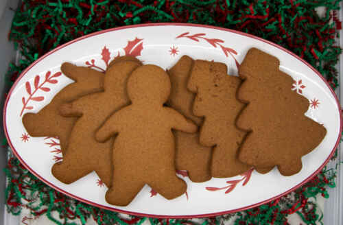 A plate of six gingerbread cookies in the shape of gingerbread people and trees.