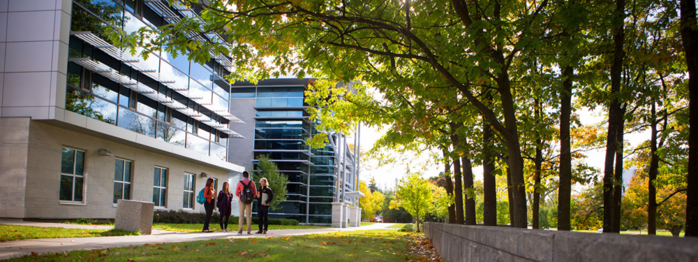 A group of four students stand and chat in front of a building on the U of G campus.
