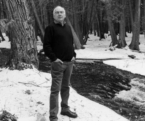 Black and white photo of a man standing near a forest stream in winter
