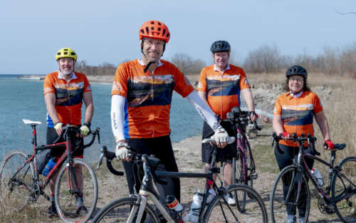 four people in biking gear pose on a beach with their bikes