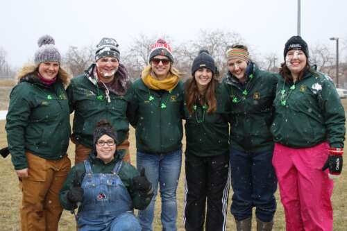 A group of students wearing matching green coats pose together outdoors on a winter day.