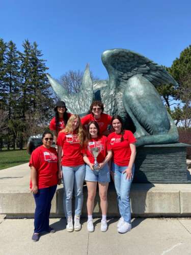 Giving games volunteers pose wearing matching red shirts in front of the Gryphon statue.
