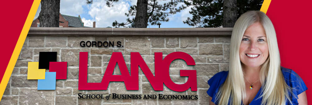 Dr. Sara Mann in front of the Gordon S. Lang School of Business and Economics brick wall sign.