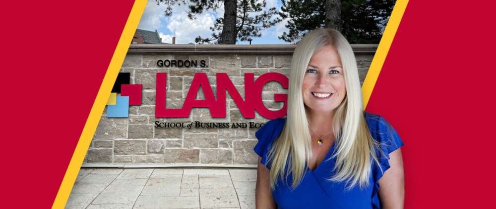 Dr. Sara Mann in front of the Gordon S. Lang School of Business and Economics brick wall sign.