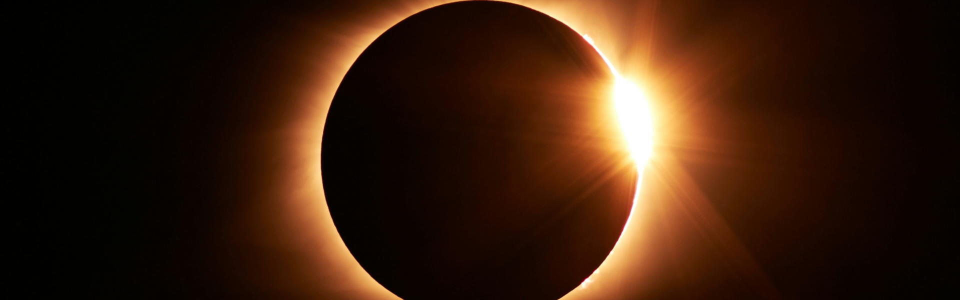Eclipse in a dark sky, sunlight peeking behind a dark circular object