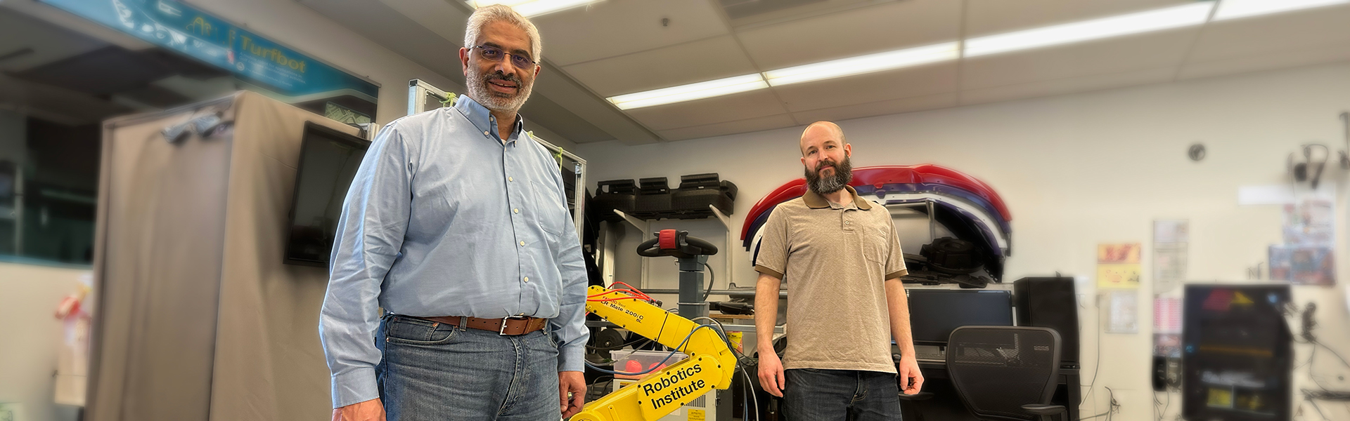 Dr. Medhat Moussa and Cole Tarry standing beside yellow arm of robot