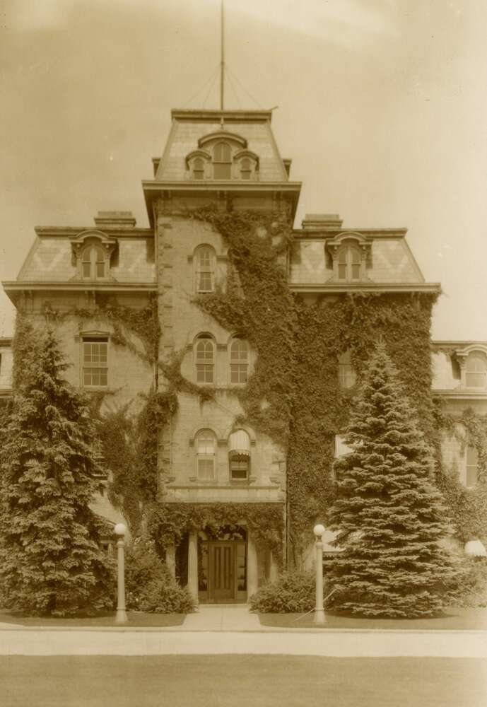 Black and white photo of Moreton Lodge in 1900. The building is tower-like, covered with greenery, surrounded by trees