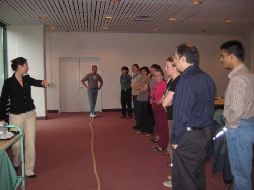 Participants engage in the personal leadership at work workshop. They stand in a line parallel to a piece of rope laid out on the ground listening to instructions.