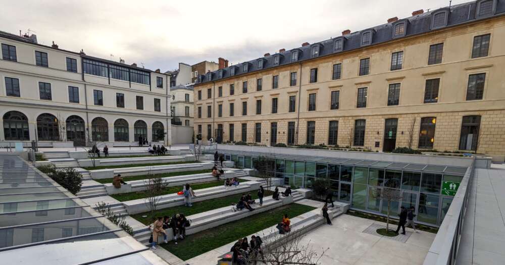 A view of two long Parisian buildings with steps down in a grassy courtyard