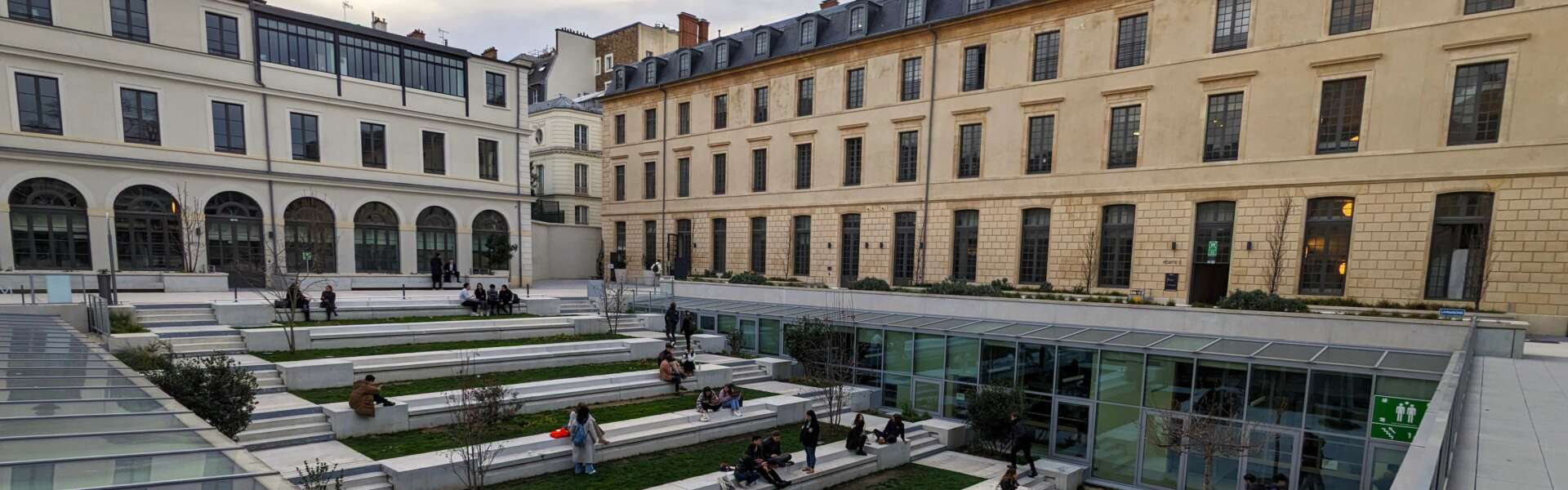 A view of two long Parisian buildings with steps down in a grassy courtyard