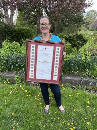 Shannon stands outside in front of greenery holding a large award.