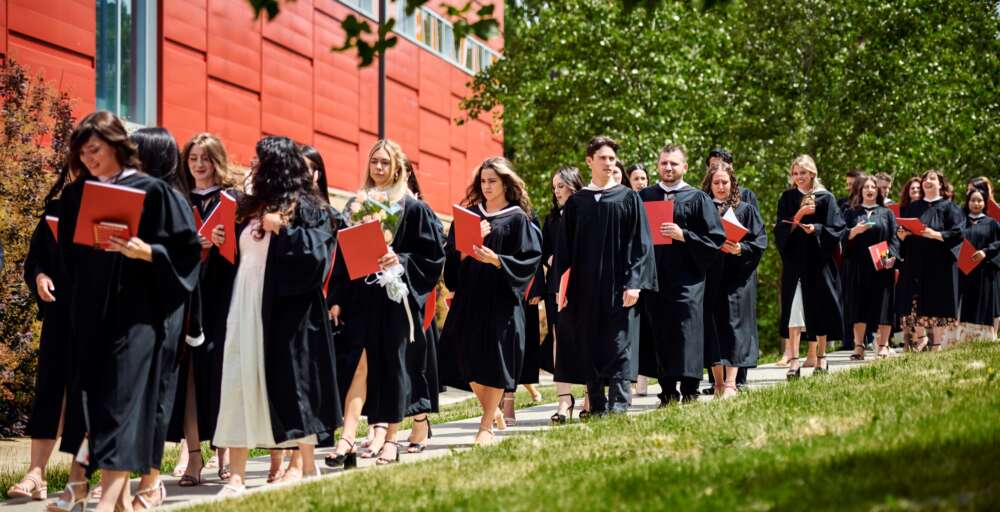 Graduates with degrees walk along an outdoor path after convocation