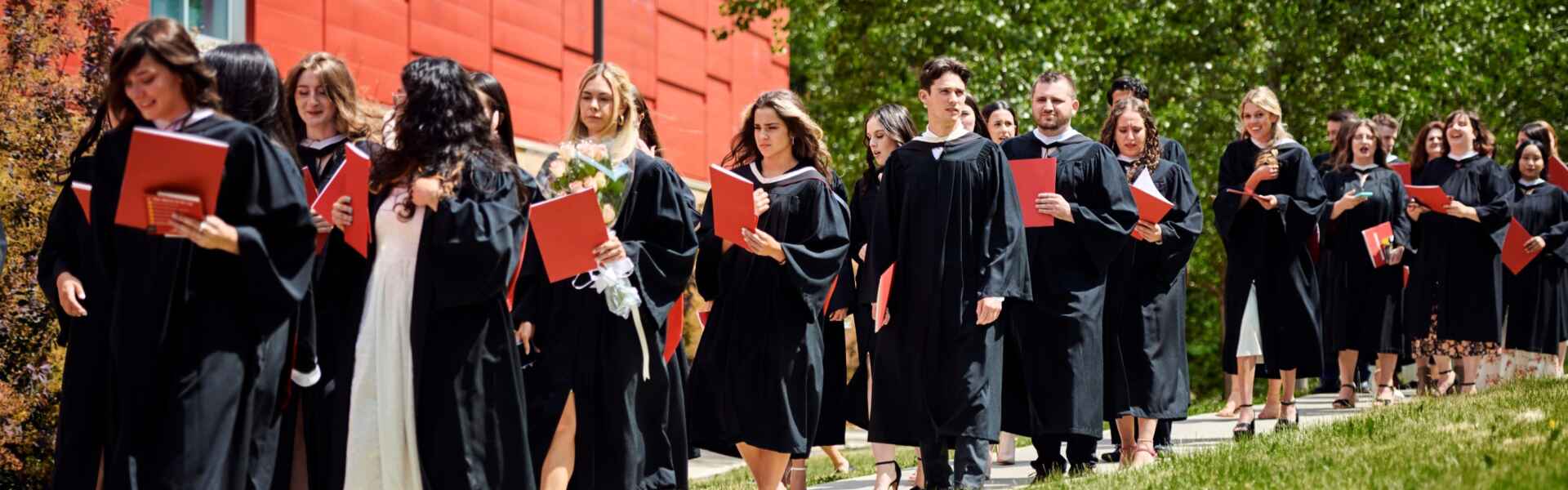 Graduates with degrees walk along an outdoor path after convocation