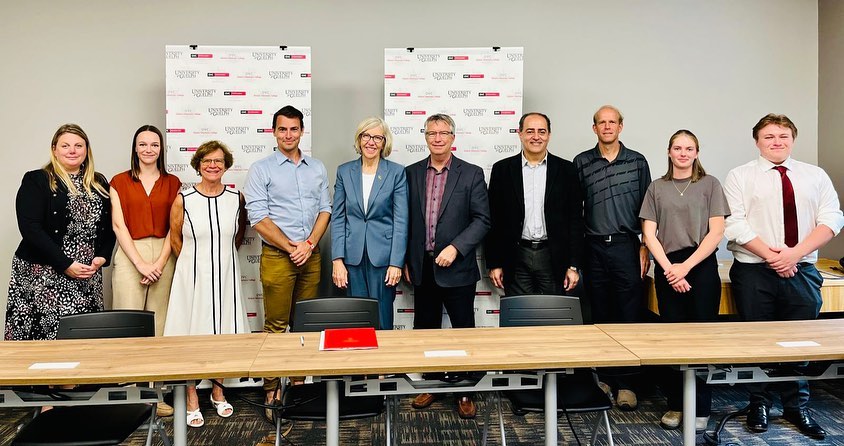 A row of people standing behind a long table, including Benjamin Snetsinger (right) pictured with MPs Adam van Koeverden and Lloyd Longfield, as well as U of G faculty, at roundtable discussion