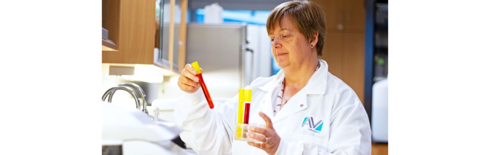 A person in a lab coat stands in a lab and pulls out test tubes filled with coloured liquids from a tube holder