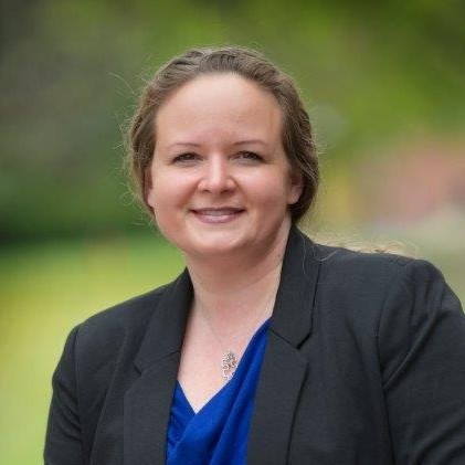 Jennifer Ellis wearing a black blazer and blue shirt, sitting outside.