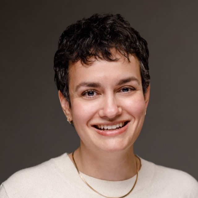 Rebecca Shapiro smiles at the camera, wearing a white sweater and a gold necklace.