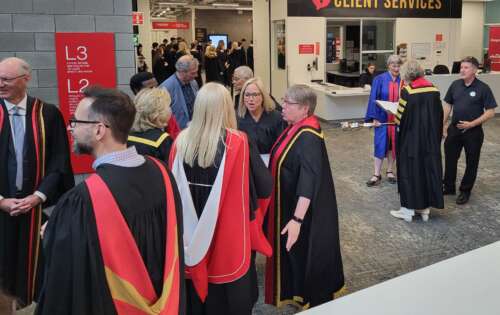 Staff and faculty wearing their convocation robes stand around talking to each other while waiting for convocation to begin.