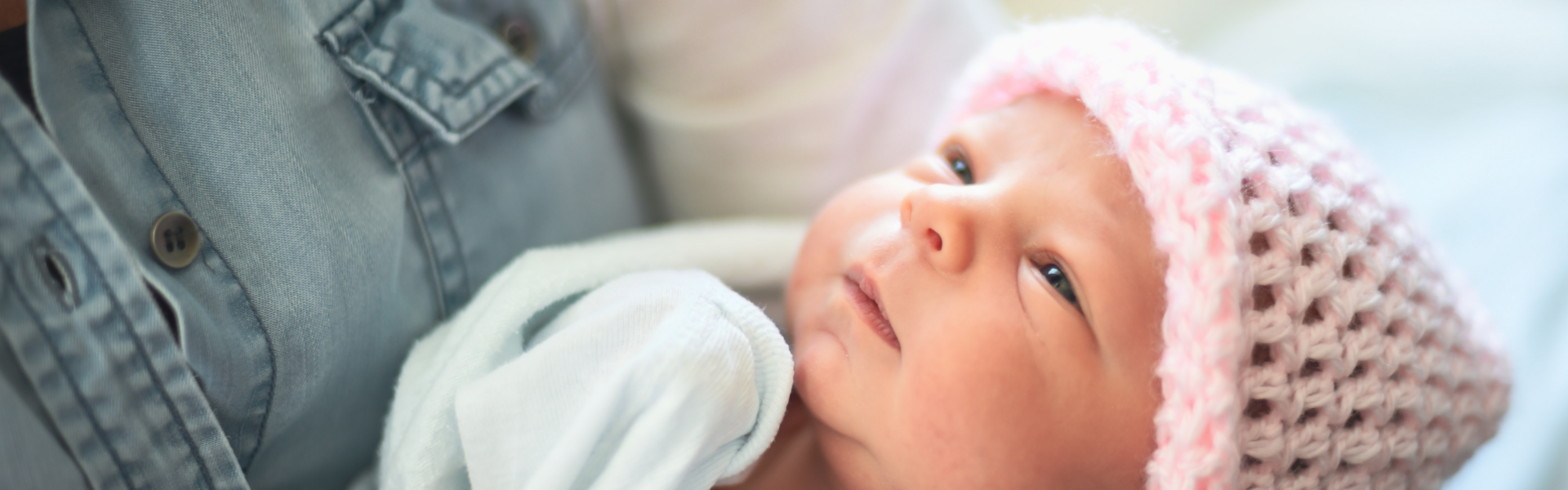 Close-up of an infant, with eyes half-shut, looking up at a person holding them who is just outside frame