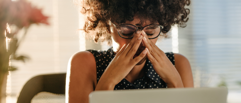 Person in front of a computer stressed with both hands on their face.