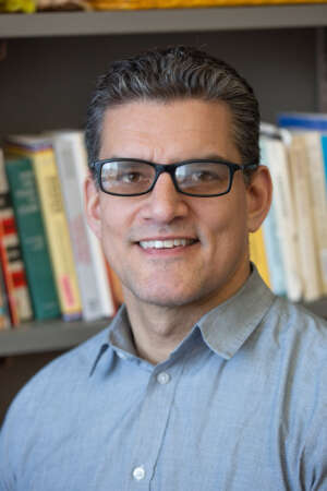 Headshot of Dr. David Fortin in front of a bookshelf, he's wearing a light-blue button up collared shirt.