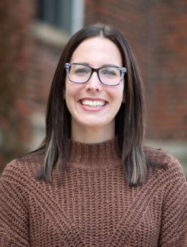 a person smiles for a portrait against a brick building