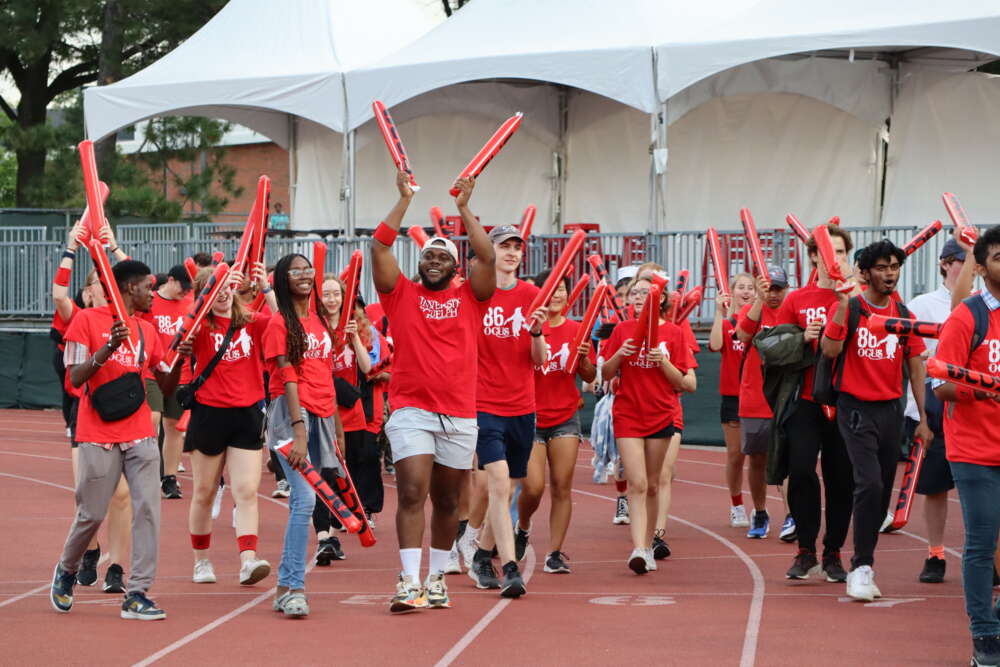 students dressed in red shirts wave their arms and walk on a track