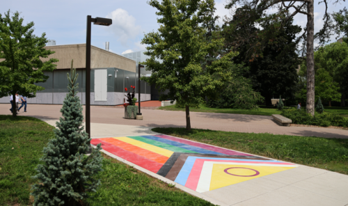 A large pride flag on a sidewalk on a sunny day