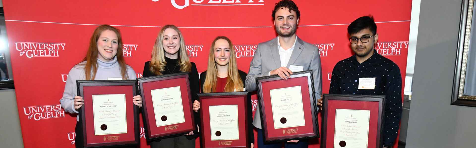 Five people holding framed award pose for a photo in front of a University of Guelph banner