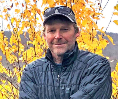 Dan Kraus stands outside in front of a tree with yellow leaves in the fall.