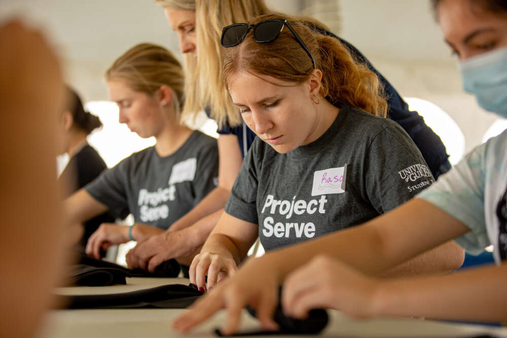 a woman with red hair wearing a grey project serve shirt works at a table surrounded by other volunteers