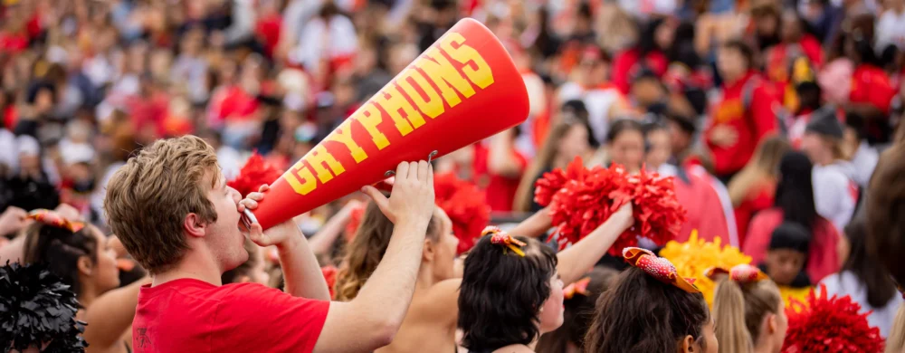 fans dressed in red cheer in the stands, one man holds a red megaphone that says gryphons