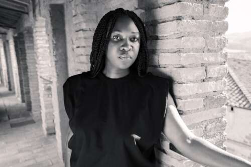 Black and white photo of Canisia posing in a brick hallway with a serious expression.