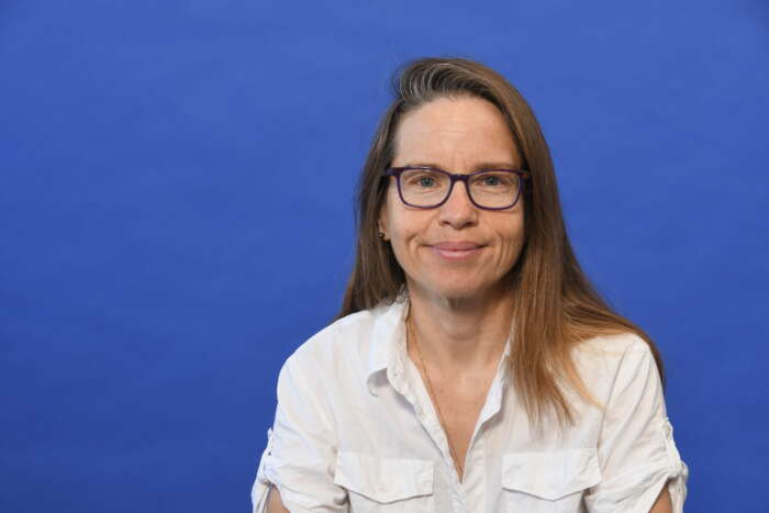 Headshot of Dr. Hélène Carabin, wearing a white button up shirt against a blue background.