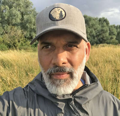 Selfie of Faisal Moola in a field wearing a jacket and a baseball hat.